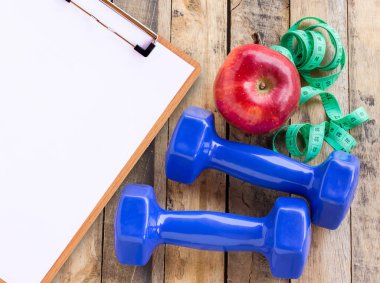 Mavi halter, beyaz havlu, ölçme bant ve ahşap masa üzerinde kırmızı elma ile tıbbi formu. Fitness kavramı