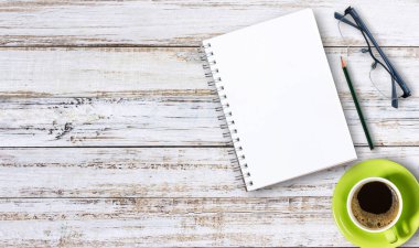 Boş not defteri, bardaklar ve kalemle ofis tahtasının üzerinde bir fincan kahve.