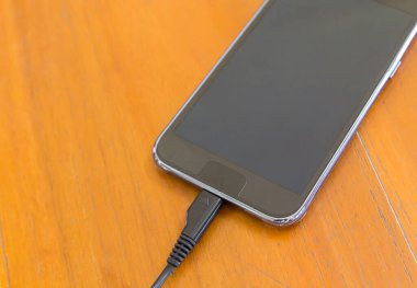Ahşap doku arka plan üzerinde Usb kablosu ile şarj akıllı telefon yakın çekim