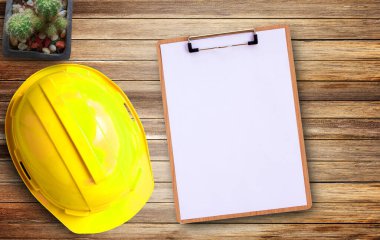 Sarı güvenlik kaskı ve işyerindeki eski kahverengi ahşap arka plan üzerine beyaz kağıt..