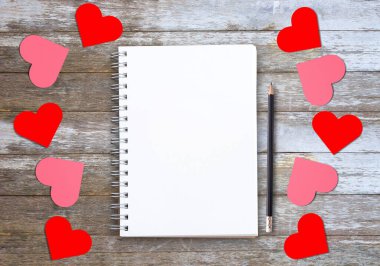 Boş defterler ya da not defterleri, kalem, kırmızı ve pembe kağıt kalp ahşap masa arkaplan üst görünümü üzerinde kopyalanmış. Aşk ve sevgililer günü konsepti.