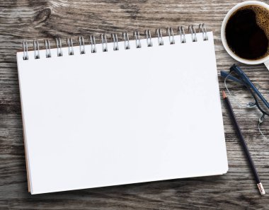 Boş defter, kurşun kalem, bardak, kahve fincanı ve iş yerindeki ahşap arka planda çiçek. Metin veya herhangi bir tasarım için kopyalama alanı olan üst görünüm.