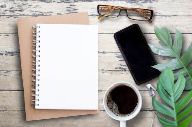 Not defteri, akıllı telefon, bardaklar, kahve fincanı ve ahşap masa arkasında yeşil izin. Herhangi bir tasarımı kopyala.