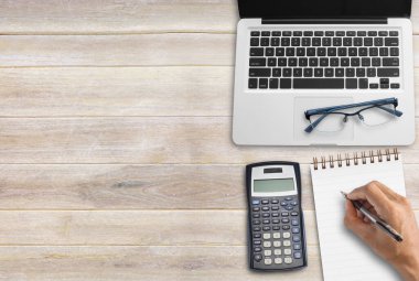 Ofis masrafları için bütçe hesaplamasını kapat. İş ve finansal konsept. Ofis masasında dizüstü bilgisayar, defter, hesap makinesi ve ahşap masa arkaplanı var. Kopyalama alanı olan üst görünüm.