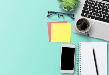 Ofis masası Düz açılı dizüstü bilgisayar klavyesi, bir kupa kahve, yeşil kaktüs ve yeşil masa arkaplanındaki boş spiral kopya defteri. Tasarım için boşluk.