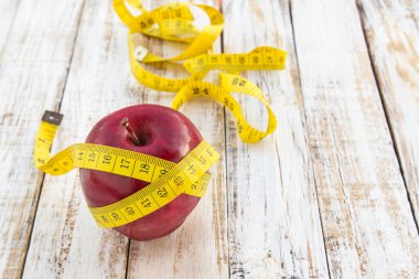 Kırmızı elma ve bir beyaz ahşap masa arka planda sarı şerit metre. Sağlıklı diyet ve vücut kilo kontrolü için kavram.