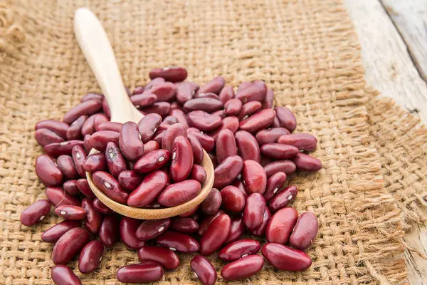 Tahta kaşık çuvala ahşap masa arka plan üzerinde kırmızı fasulye