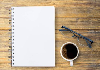 Boş defter, bardaklar ve kahve ofis işyerindeki kahverengi ahşap masada. Tasarımınız için kopyalama alanı olan en üst görünüm.