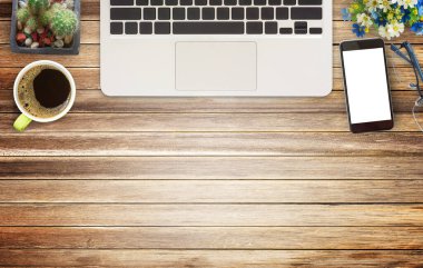 Ofis resepsiyon masası Büro düzenlemeleri, dizüstü bilgisayar, gözlük, akıllı telefon, fincan kahve ve ahşap masa arka plan üzerinde çiçek ile. Kopya alanı (seçici odak ile Üstten Görünüm)