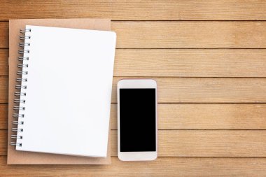 Düz boş kağıt defter ve kahverengi ahşap masa arkaplan üzerine akıllı telefon eğitim tanıtım reklamları konsepti. Fotokopi alanı olan üst görünüm (seçici odaklı). Ofis masası konsepti.