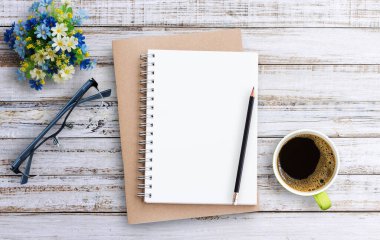 Ofis malzemeleri, not defteri, bardaklar, bir fincan kahve ve tahta arka planda siyah kalemle birlikte düz bir ahşap ofis masası. Kopya alanı (seçici odak) olan üst görünüm. Ofis masası ve iş konsepti.