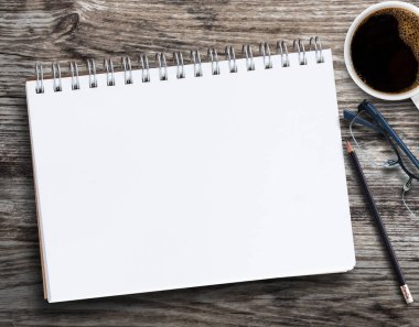 Boş defter, kurşun kalem, bardak, kahve fincanı ve iş yerindeki ahşap arka planda çiçek. Metin veya herhangi bir tasarım için kopyalama alanı olan üst görünüm.