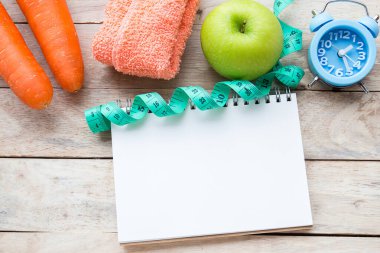 Üstten görünüm havuç ile mavi stetoskop, bant, elma, çalar saat ve ahşap masa arka plan üstünde defter ölçme. Diyet ve sağlık, beslenme ve sağlık sigortası kavramı