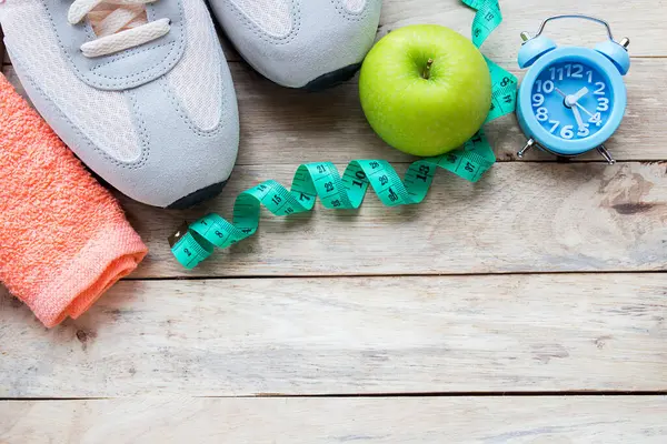 Üstten görünüm ayakkabı, bant, yeşil elma, çalar saat ve ahşap masa arka plan havluda ölçme. Diyet ve sağlık, beslenme ve sağlık sigortası kavramı