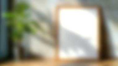 Bereketli yeşil bir bitkinin yanında boş bir çerçeve içeren sakin bir iç mekan, doğal güneş ışığıyla aydınlatılmış, ev dekorasyonu için mükemmel bir sakinleştirici atmosfer yaratıyor..