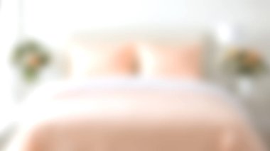 Yumuşak, bulanık bir yatak odası görüntüsü. Açık renkli yatak ve dekoratif öğeler var. Huzurlu ve rahatlatıcı bir ortam yaratıyor..