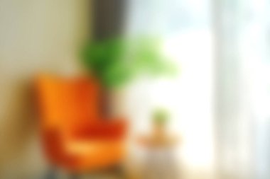 Güneşli bir pencerenin yanında parlak turuncu bir sandalye bulunan rahat bir oturma odası. Sahne yumuşak bir ışık ve küçük bir saksı bitkisi içeriyor, davetkar bir atmosfer yaratıyor..