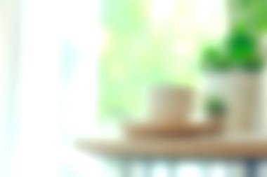 Yeşil bitkilerin yanındaki ahşap bir masaya yerleştirilmiş yumuşak odaklı kahve fincanının olduğu sakin bir sahne, rahat bir sabah ortamının özünü yakalıyor..