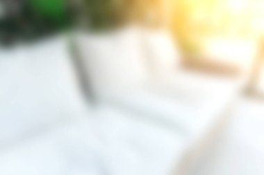 Sıcak güneş ışığıyla yıkanmış rahat beyaz bir kanepenin bulanık görüntüsü, yeşilliklerle çevrili, dinlenmek için ideal, sakin bir kapalı atmosfer yaratıyor..