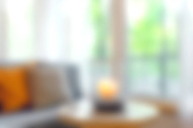 Huzurlu bir oturma odası manzarası yumuşak ışıklandırması, bulanık yeşil manzaralı rahat bir atmosfer ve rahatlamak için ideal sıcak bir mum süsü sergiliyor..