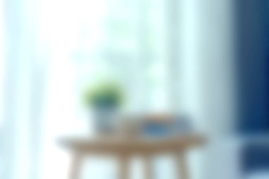 Bu yumuşak odak görüntüsü, perdelerin arasından süzülen doğal ışıkla dolu rahat bir yaşam alanı yakalar, saksı bitkisi ve dekoratif elementlerle süslenmiş ahşap bir tabloyu renklendirir, sakin bir atmosfer yaratır..