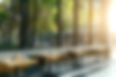 Ağaçların arasından süzülen yumuşak güneş ışığıyla yemyeşil masaların olduğu sıcak ve davetkar bir açık kafe. Huzurlu bir atmosfer yaratıyor..