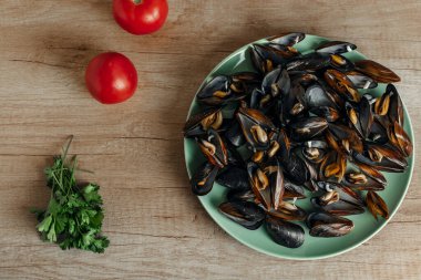 Tahta tabakta taze midye, domates ve maydanoz manzaralı.