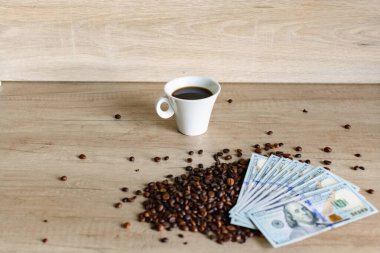 Yakın plan kahve çekirdekleri, bir fincan sade kahve ve ahşap bir masada Amerikan dolarları. Zenginlik, iş başarısı, kahve ticareti ve lüks yaşam tarzı kavramı.