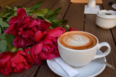 Latte sanatıyla romantik bir sabah kahvesi ve ahşap masada taze kırmızı şakayıklar.