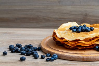 Tatlı sabah lezzeti: yaban mersinli ve şekerli ince krepler. Yaban mersini ve pudra şekeriyle süslenmiş, ahşap tabakta duran altın ince krepler. Taze pişmiş ev yemeği, geleneksel tatlı kahvaltı fikri.