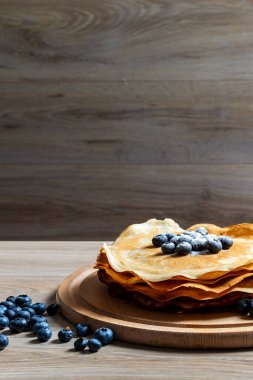 Tatlı sabah lezzeti: yaban mersinli ve şekerli ince krepler. Yaban mersini ve pudra şekeriyle süslenmiş, ahşap tabakta duran altın ince krepler. Taze pişmiş ev yemeği, geleneksel tatlı kahvaltı fikri.