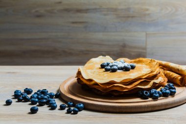 Tatlı sabah lezzeti: yaban mersinli ve şekerli ince krepler. Yaban mersini ve pudra şekeriyle süslenmiş, ahşap tabakta duran altın ince krepler. Taze pişmiş ev yemeği, geleneksel tatlı kahvaltı fikri.