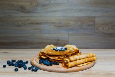 Tatlı sabah lezzeti: yaban mersinli ve şekerli ince krepler. Yaban mersini ve pudra şekeriyle süslenmiş, ahşap tabakta duran altın ince krepler. Taze pişmiş ev yemeği, geleneksel tatlı kahvaltı fikri.