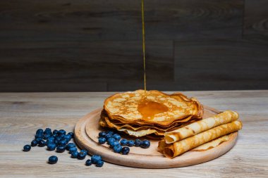 Tatlı sabah lezzeti: yaban mersinli ve şekerli ince krepler. Yaban mersini ve pudra şekeriyle süslenmiş, ahşap tabakta duran altın ince krepler. Taze pişmiş ev yemeği, geleneksel tatlı kahvaltı fikri.