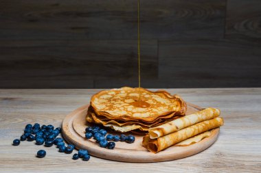 Tatlı sabah lezzeti: yaban mersinli ve şekerli ince krepler. Yaban mersini ve pudra şekeriyle süslenmiş, ahşap tabakta duran altın ince krepler. Taze pişmiş ev yemeği, geleneksel tatlı kahvaltı fikri.