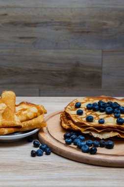 Tatlı sabah lezzeti: yaban mersinli ve şekerli ince krepler. Yaban mersini ve pudra şekeriyle süslenmiş, ahşap tabakta duran altın ince krepler. Taze pişmiş ev yemeği, geleneksel tatlı kahvaltı fikri.