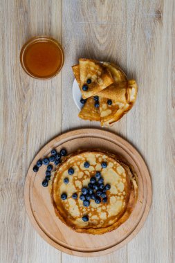 Tatlı sabah lezzeti: yaban mersinli ve şekerli ince krepler. Yaban mersini ve pudra şekeriyle süslenmiş, ahşap tabakta duran altın ince krepler. Taze pişmiş ev yemeği, geleneksel tatlı kahvaltı fikri.