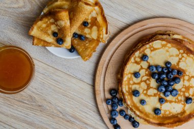 Tatlı sabah lezzeti: yaban mersinli ve şekerli ince krepler. Yaban mersini ve pudra şekeriyle süslenmiş, ahşap tabakta duran altın ince krepler. Taze pişmiş ev yemeği, geleneksel tatlı kahvaltı fikri.