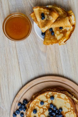 Tatlı sabah lezzeti: yaban mersinli ve şekerli ince krepler. Yaban mersini ve pudra şekeriyle süslenmiş, ahşap tabakta duran altın ince krepler. Taze pişmiş ev yemeği, geleneksel tatlı kahvaltı fikri.