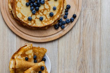 Tatlı sabah lezzeti: yaban mersinli ve şekerli ince krepler. Yaban mersini ve pudra şekeriyle süslenmiş, ahşap tabakta duran altın ince krepler. Taze pişmiş ev yemeği, geleneksel tatlı kahvaltı fikri.