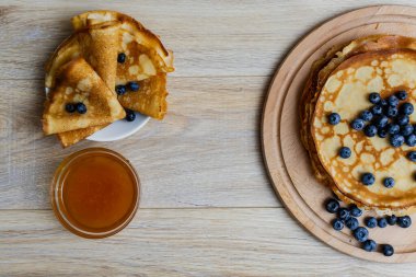 Tatlı sabah lezzeti: yaban mersinli ve şekerli ince krepler. Yaban mersini ve pudra şekeriyle süslenmiş, ahşap tabakta duran altın ince krepler. Taze pişmiş ev yemeği, geleneksel tatlı kahvaltı fikri.