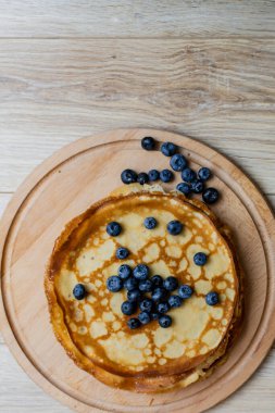 Tatlı sabah lezzeti: yaban mersinli ve şekerli ince krepler. Yaban mersini ve pudra şekeriyle süslenmiş, ahşap tabakta duran altın ince krepler. Taze pişmiş ev yemeği, geleneksel tatlı kahvaltı fikri.