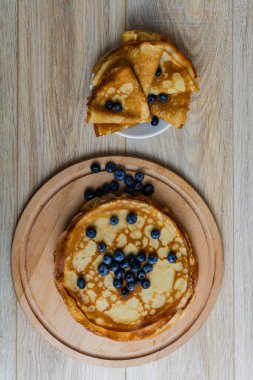 Tatlı sabah lezzeti: yaban mersinli ve şekerli ince krepler. Yaban mersini ve pudra şekeriyle süslenmiş, ahşap tabakta duran altın ince krepler. Taze pişmiş ev yemeği, geleneksel tatlı kahvaltı fikri.