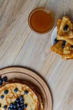 Tatlı sabah lezzeti: yaban mersinli ve şekerli ince krepler. Yaban mersini ve pudra şekeriyle süslenmiş, ahşap tabakta duran altın ince krepler. Taze pişmiş ev yemeği, geleneksel tatlı kahvaltı fikri.