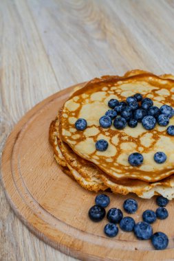 Tatlı sabah lezzeti: yaban mersinli ve şekerli ince krepler. Yaban mersini ve pudra şekeriyle süslenmiş, ahşap tabakta duran altın ince krepler. Taze pişmiş ev yemeği, geleneksel tatlı kahvaltı fikri.