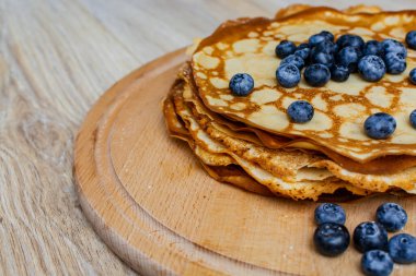 Tatlı sabah lezzeti: yaban mersinli ve şekerli ince krepler. Yaban mersini ve pudra şekeriyle süslenmiş, ahşap tabakta duran altın ince krepler. Taze pişmiş ev yemeği, geleneksel tatlı kahvaltı fikri.