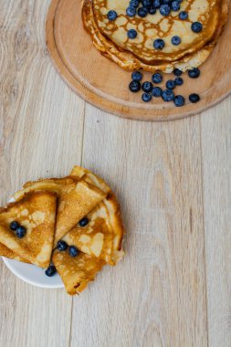 Tatlı sabah lezzeti: yaban mersinli ve şekerli ince krepler. Yaban mersini ve pudra şekeriyle süslenmiş, ahşap tabakta duran altın ince krepler. Taze pişmiş ev yemeği, geleneksel tatlı kahvaltı fikri.