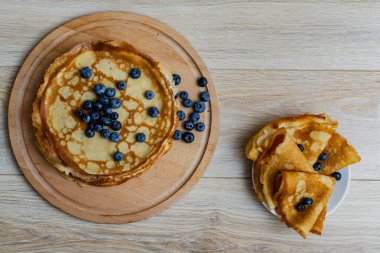 Tatlı sabah lezzeti: yaban mersinli ve şekerli ince krepler. Yaban mersini ve pudra şekeriyle süslenmiş, ahşap tabakta duran altın ince krepler. Taze pişmiş ev yemeği, geleneksel tatlı kahvaltı fikri.