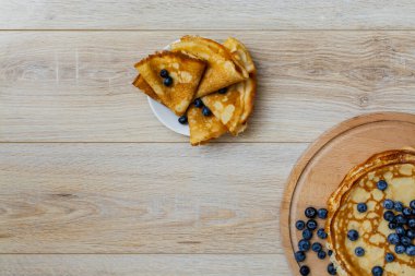 Tatlı sabah lezzeti: yaban mersinli ve şekerli ince krepler. Yaban mersini ve pudra şekeriyle süslenmiş, ahşap tabakta duran altın ince krepler. Taze pişmiş ev yemeği, geleneksel tatlı kahvaltı fikri.