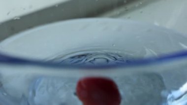 Yavaş çekimde suya sıçrayan kiraz domateslerinin yakın plan görüntüsü. Kırmızı kirazlı domateslerin suya düşüşü. Canlı sıçrama ve yükselen kabarcıklarla yüksek hızlı atış. Mutfak ve sağlık görüntüleri için mükemmel..